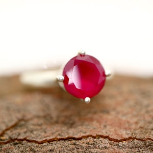 May include: A silver ring with a large, faceted, red gemstone.