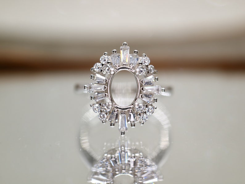 Puede incluir: Un anillo de plata con un engaste ovalado grande rodeado de piedras redondas y baguette m&aacute;s peque&ntilde;as.
