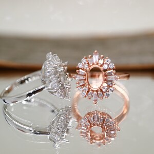 Puede incluir: Dos anillos con piedras transparentes. El anillo de la izquierda tiene una banda plateada y una piedra grande de forma ovalada rodeada de piedras m&aacute;s peque&ntilde;as. El anillo de la derecha tiene una banda de oro rosa y un engaste grande de forma ovalada rodeado de piedras m&aacute;s peque&ntilde;as.