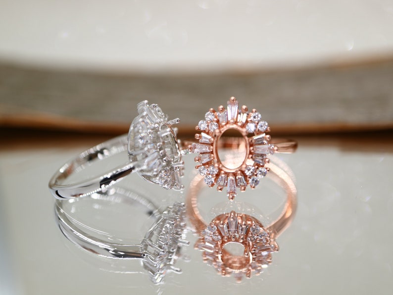 Puede incluir: Dos anillos con piedras transparentes. El anillo de la izquierda tiene una banda plateada y una piedra grande de forma ovalada rodeada de piedras m&aacute;s peque&ntilde;as. El anillo de la derecha tiene una banda de oro rosa y un engaste grande de forma ovalada rodeado de piedras m&aacute;s peque&ntilde;as.