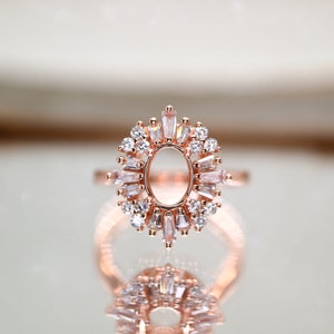 Puede incluir: Un anillo de oro rosa con una gran piedra ovalada central rodeada de piedras m&aacute;s peque&ntilde;as de forma baguette.