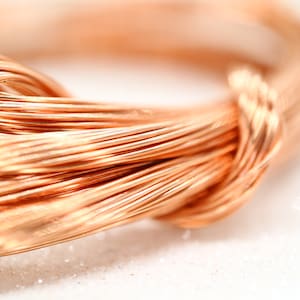 Può includere: Primo piano di una bobina di filo di rame. Il filo è di un colore marrone rossastro caldo e sembra essere avvolto strettamente. L'immagine è ben illuminata, evidenziando la consistenza e la lucentezza del metallo. Il filo è probabilmente utilizzato per scopi elettrici o artigianali.