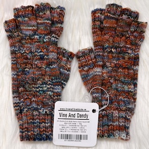 May include: Fingerless gloves in a multi-coloured knit pattern, with brown, orange, blue, and grey hues. The gloves have a tag that reads "Vine And Dandy". The gloves are displayed on a white, fluffy surface.