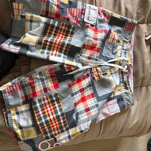 May include: Gray, red, yellow, and white patchwork swim trunks with a drawstring waist. The trunks feature a variety of plaid and patterned fabric squares. The brand name "SIX EIGHT SIX" is visible on the right side of the trunks.