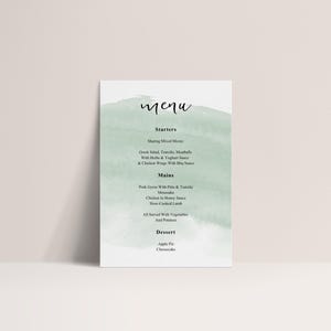May include: A white menu card with a watercolor wash of pale green. The word "menu" is written in elegant script at the top. The menu lists starters, mains, and dessert options, including Greek salad and apple pie.
