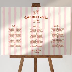 May include: A wedding seating plan displayed on an easel. The sign features a pink and white striped design with the words "take your seats" in red script. Guest names are listed under table numbers.