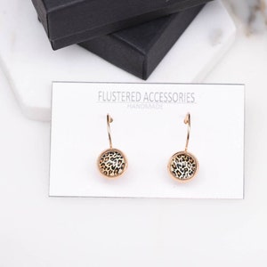 May include: Gold hoop earrings with a round, leopard print design. The earrings are handmade and feature a simple, elegant style.