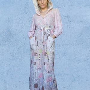 May include: A long, quilted robe with a hood, featuring a patchwork design in shades of pink, white, and brown. The robe has a zipper closure, pockets, and a matching belt. The sleeves are long, and the robe appears to be made of a soft, comfortable material.