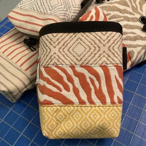 May include: A multi-colored climbing chalk bag with a black drawstring and a geometric pattern. The bag is made of a durable fabric and has a variety of colors, including beige, orange, and yellow.