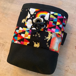 May include: A black climbing chalk bag with a colorful patchwork design featuring unicorns, rainbows, and stars. The bag has a drawstring closure with a black toggle.