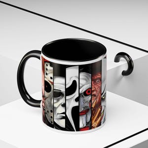 Puede incluir: Una taza de cerámica con interior y asa negros, que presenta un estampado gráfico envolvente de varios rostros de personajes de películas de terror dispuestos en paneles verticales, incluyendo una máscara de hockey y una cara de payaso.