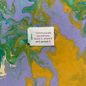 May include: Abstract painting with swirls of yellow, green, and purple paint. A white tag with the text "Communicate sacredness; build it, share it and spread it." is attached to the painting.