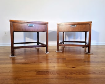May include: Two matching wooden end tables with a single drawer and a lower shelf. The tables are a dark brown color and have a simple, mid-century modern design.