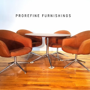 May include: A set of four swivel chairs with orange upholstery and chrome bases surrounding a round wooden table. The chairs and table are arranged in a square formation. The text "PROREFINE FURNISHINGS" is visible on the wall behind the furniture.