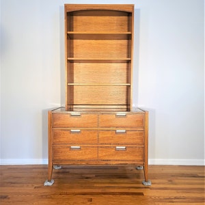 May include: A wooden dresser with six drawers and a matching bookcase with four shelves. The dresser has a glass top and the bookcase has a curved top.