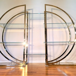 May include: A set of two gold metal and glass shelves with a curved design. The shelves are freestanding and have multiple tiers.