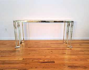 May include: A gold metal console table with a rectangular glass top and a geometric design on the legs.