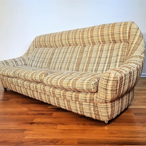 May include: A brown and beige plaid sofa with a curved back and armrests. The sofa is sitting on a wooden floor.