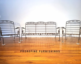May include: A set of three wrought iron patio furniture pieces, including a loveseat and two armchairs. The furniture is made of black metal with intricate scrollwork details. The furniture is sitting on a wooden floor.