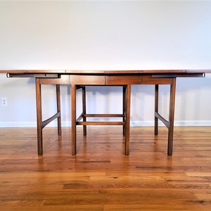 May include: A brown wooden extendable dining table with a rectangular top and four legs. The table has a simple design with a smooth finish.