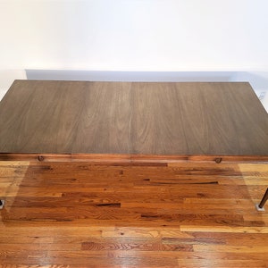 May include: A brown wooden dining table with a rectangular top and four legs. The table is made of wood with a natural finish. The table is sitting on a wooden floor.