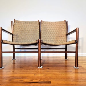 May include: A mid-century modern two-seater sofa with a woven rope seat and a dark wood frame. The sofa has a simple design with straight lines and a low profile.