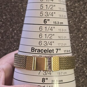 May include: A gold-toned metal watch bracelet being measured on a white measuring tape with markings in inches and centimeters. The bracelet is 7 inches or 17.8 centimeters long.