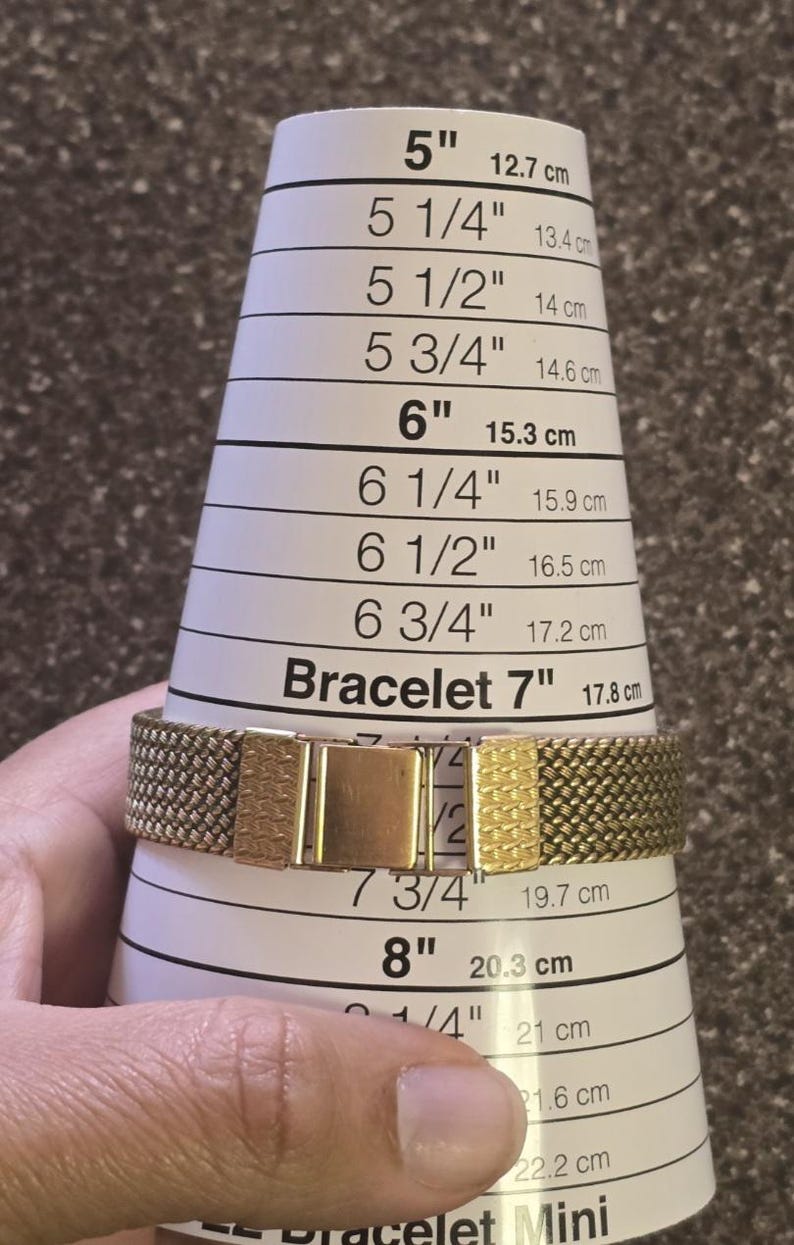 May include: A gold-toned metal watch bracelet being measured on a white measuring tape with markings in inches and centimeters. The bracelet is 7 inches or 17.8 centimeters long.
