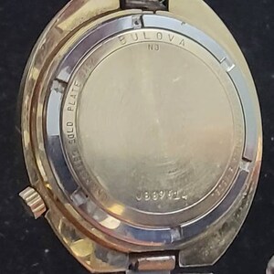 K&ouml;nnte beinhalten: Die R&uuml;ckseite einer vergoldeten Bulova-Uhr mit dem Text "Bulova" und "Gold Plate", der auf den Geh&auml;useboden graviert ist. Die Uhr hat die Seriennummer "J889144".