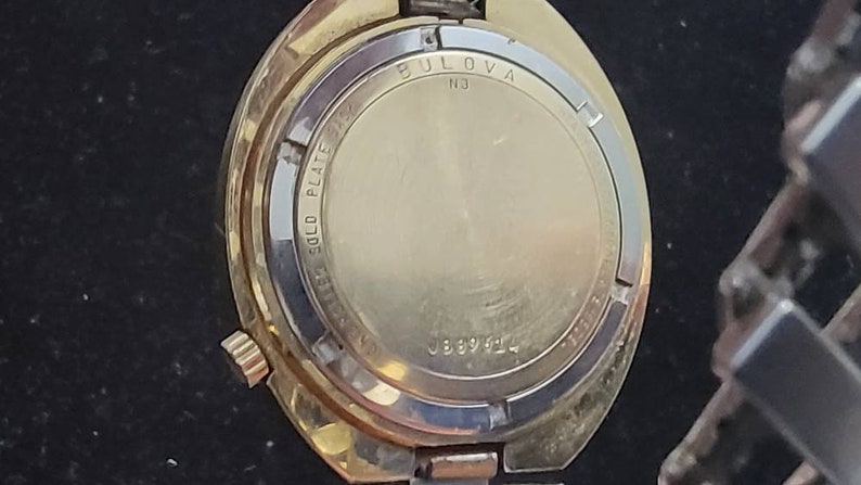 K&ouml;nnte beinhalten: Die R&uuml;ckseite einer vergoldeten Bulova-Uhr mit dem Text "Bulova" und "Gold Plate", der auf den Geh&auml;useboden graviert ist. Die Uhr hat die Seriennummer "J889144".
