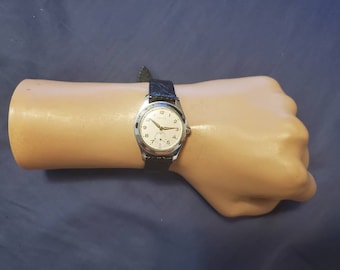 May include: A silver wristwatch with a white face and black leather band. The watch face has black Roman numeral hour markers and black hands. The watch face also has a small seconds dial at the 6 o'clock position.