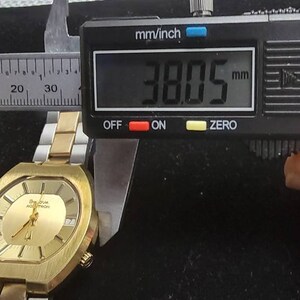 K&ouml;nnte beinhalten: Eine goldfarbene Uhr mit quadratischem Zifferblatt und einem Metallband. Die Uhr wird mit einer Schieblehre gemessen, die 38,05 mm anzeigt.