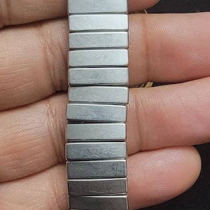 K&ouml;nnte beinhalten: Ein silbernes und goldenes Armband mit zweifarbigem Design. Das Armband besteht aus Metallgliedern und hat eine polierte Oberfl&auml;che.
