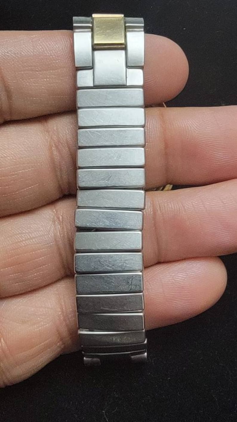 K&ouml;nnte beinhalten: Ein silbernes und goldenes Armband mit zweifarbigem Design. Das Armband besteht aus Metallgliedern und hat eine polierte Oberfl&auml;che.