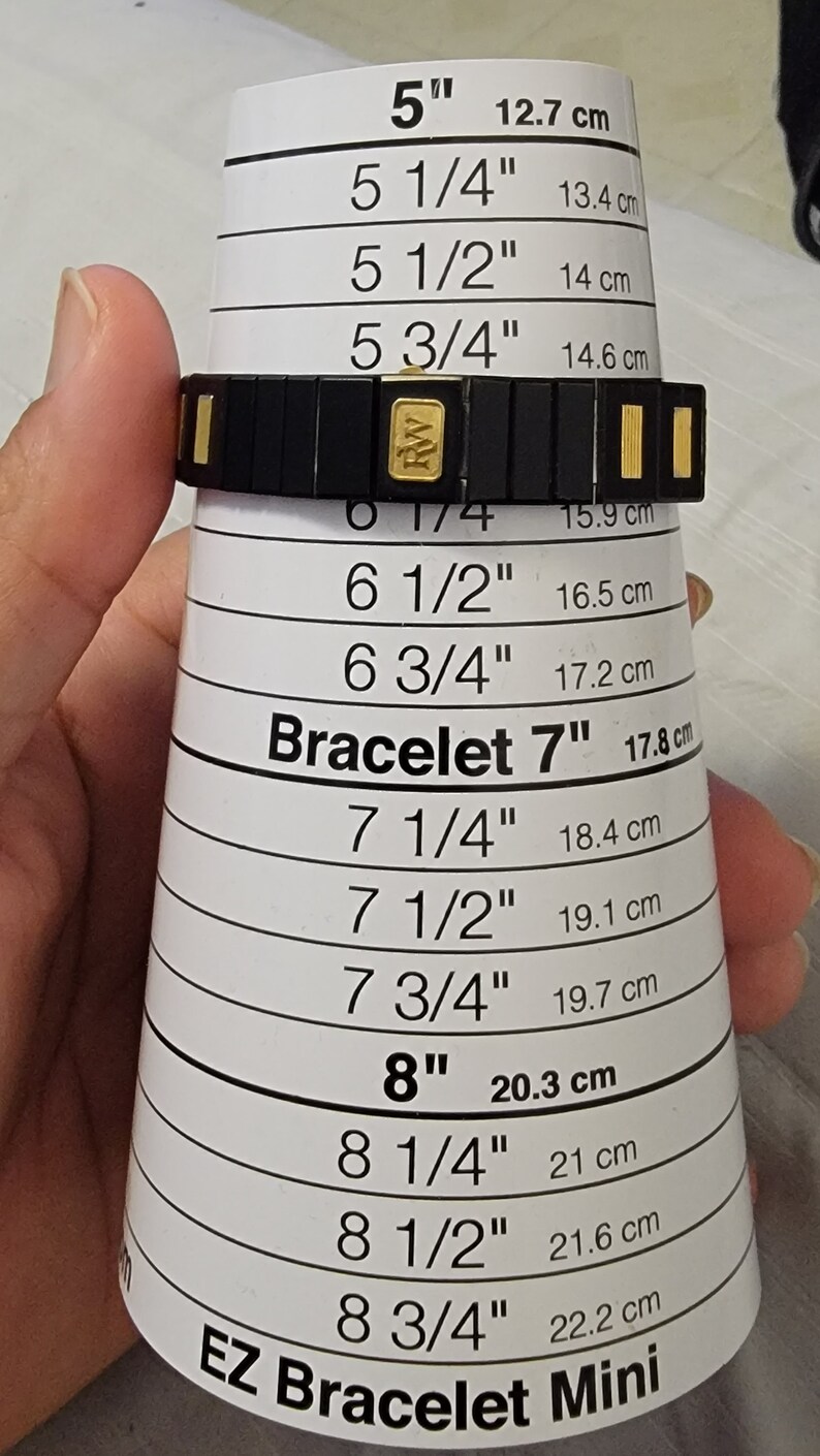 May include: A black and gold bracelet with a size guide in inches and centimeters. The guide shows sizes from 5 inches to 8 3/4 inches. The bracelet is made of black metal with gold accents. The text "EZ Bracelet Mini" is printed on the guide.