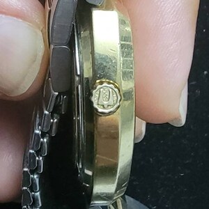 K&ouml;nnte beinhalten: Eine goldfarbene Armbanduhr mit einem silbernen Metallband. Das Zifferblatt der Uhr ist auf dem Bild nicht zu sehen. Die Uhr hat ein Logo an der Seite, auf dem "U" mit einer Krone dar&uuml;ber steht.