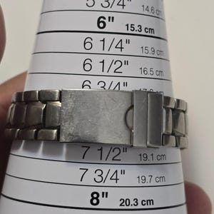 Puede incluir: Una pulsera de reloj de metal plateado con un cierre. La pulsera se est&aacute; midiendo con una regla con marcas en pulgadas y cent&iacute;metros. La pulsera mide 7 1/2 pulgadas o 19,1 cent&iacute;metros.