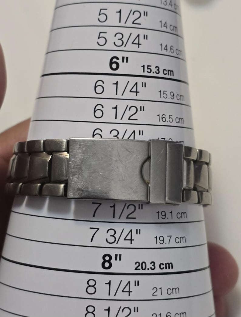 Puede incluir: Una pulsera de reloj de metal plateado con un cierre. La pulsera se est&aacute; midiendo con una regla con marcas en pulgadas y cent&iacute;metros. La pulsera mide 7 1/2 pulgadas o 19,1 cent&iacute;metros.