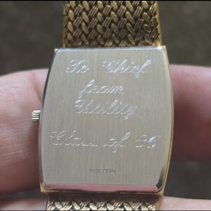 May include: Gold-tone watch with a metal band. The back of the watch has an inscription that reads "To Chief from Utility Class of '85".