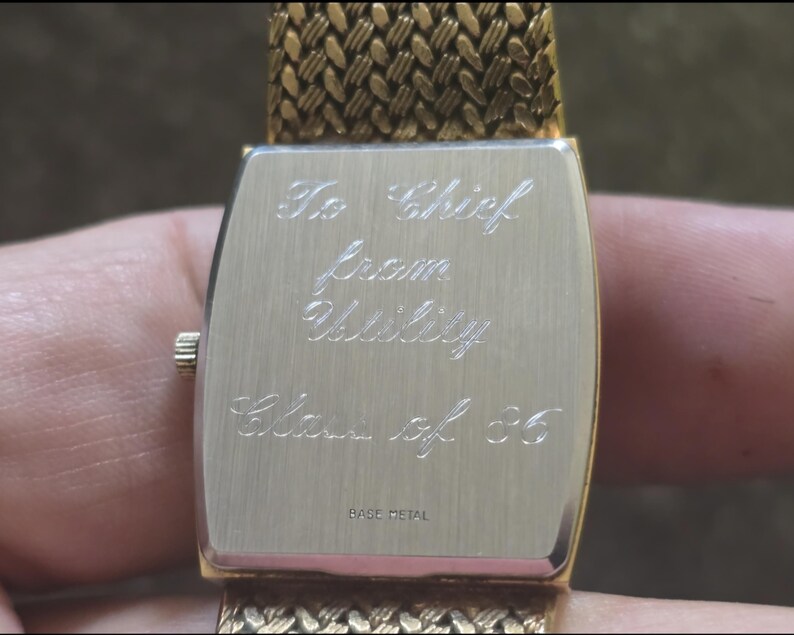 May include: Gold-tone watch with a metal band. The back of the watch has an inscription that reads "To Chief from Utility Class of '85".