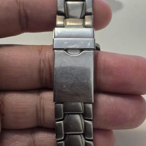 Puede incluir: Una correa de reloj de metal plateado con un cierre. La correa est&aacute; hecha de piezas de metal enlazadas.