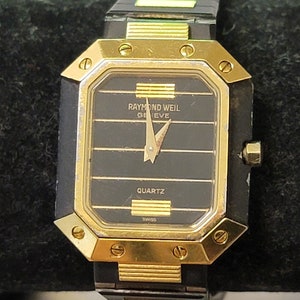 May include: A gold and black Raymond Weil Geneve quartz wristwatch with a black face and gold hands.