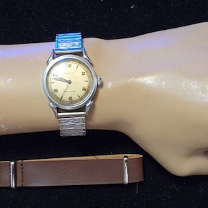 May include: A silver wristwatch with a white face and black hands. The watch is on a silver metal band. A brown leather watch strap is also pictured.
