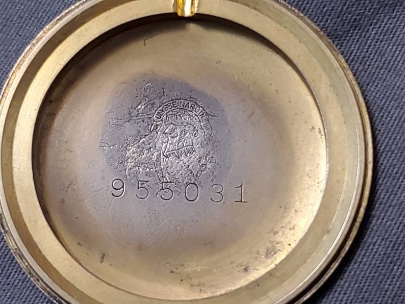 May include: Close-up of the back of a gold-toned watch. The watch has a circular case with a smooth, polished surface. The inscription "USSENARD" is visible in the center of the case, along with the number "955031".