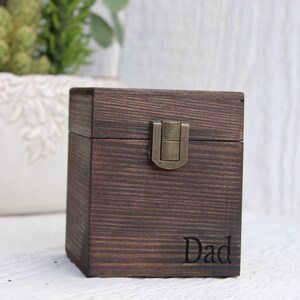 May include: A dark walnut wood box with a single compartment and a brass latch. The box is engraved with the word "Dad" in a Times font with black fill.