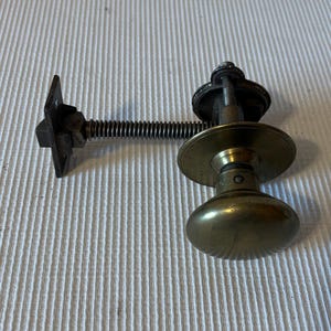 May include: A vintage brass door knob with a spring-loaded latch mechanism. The knob is round with a smooth, polished surface. The latch is attached to a metal plate with a screw.