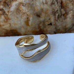 May include: A gold and white ring with a wavy design. The ring is made of two bands that are intertwined.