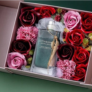 May include: A gift box filled with artificial red and pink roses and carnations, with a green glass bottle of home fragrance labelled "Citta & Sen Natural Diffuser" in the centre.