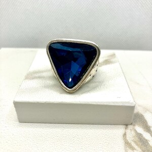 May include: A silver ring featuring a large, triangular, dark blue gemstone.