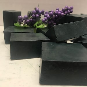 May include: A pile of black charcoal soap bars with a sprig of purple berries on top.